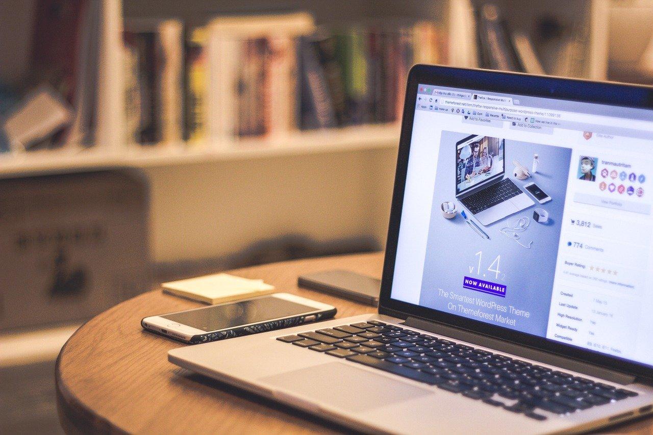 A round table in a library with a laptop, notebook, and iPhone.