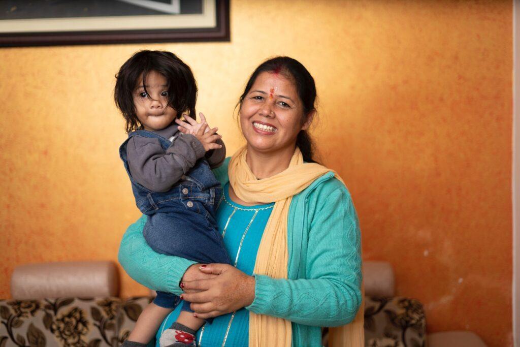 A smiling woman in a sari carries her toddler.